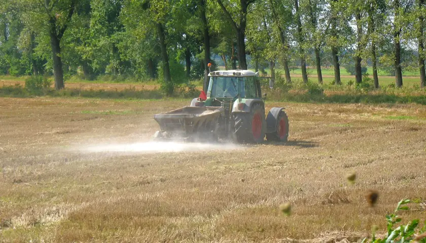 Traktor rozsypuje nawóz na polu. Wapnowanie gleby kiedy najlepiej? Jesień lub wczesna wiosna to idealny czas.